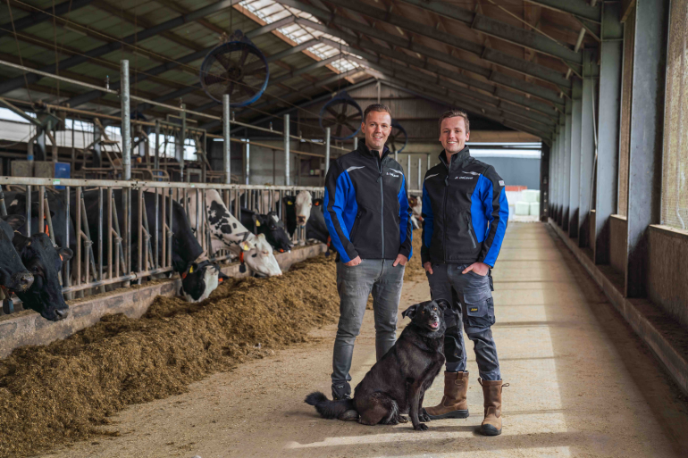 Melkveehouders van Houten met hun hond op de voergang en koeien aan het voerhek