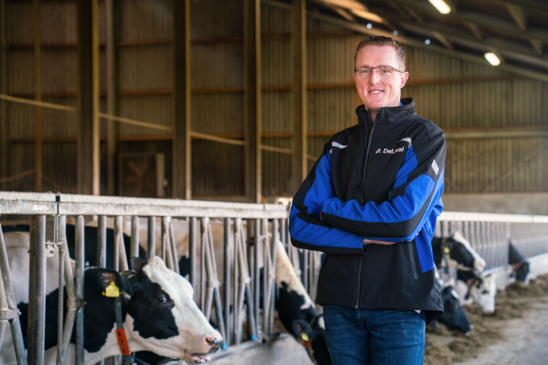 Melkveehouder Martin Brandsma met DeLaval jas in de stal met voerhek en koeien op de achtergrond