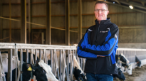Melkveehouder Martin Brandsma met DeLaval jas in de stal met voerhek en koeien op de achtergrond